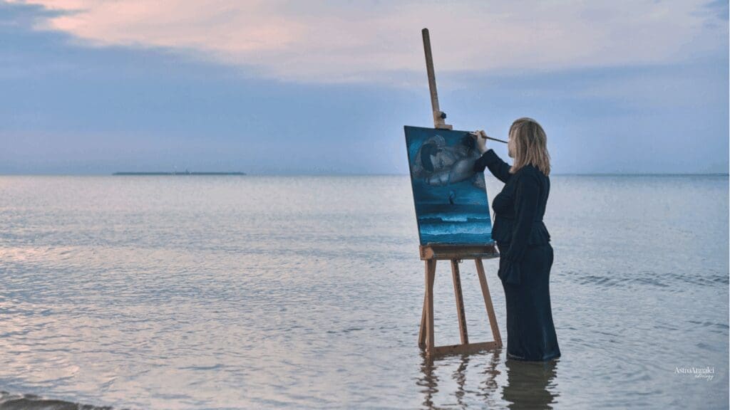 Female artist painting art in shallow part of the ocean symbolic of Neptune MC line